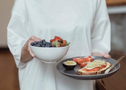 Person holding a bowl of fresh berries and a plate with avocado toast, displaying a healthy breakfast spread.